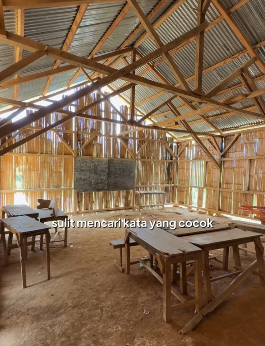 Rustic rural classroom with wooden desks and benches, chalkboard on the wall, and sunlight filtering through gaps in the wooden walls.