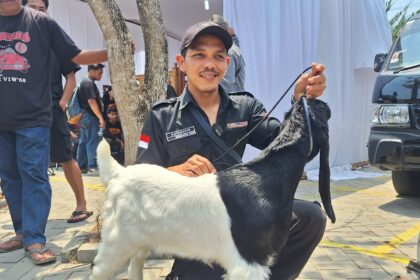 Uniformed man kneels beside a black-and-white dog on a leash at an outdoor event; Indonesian flag patch on his sleeve.