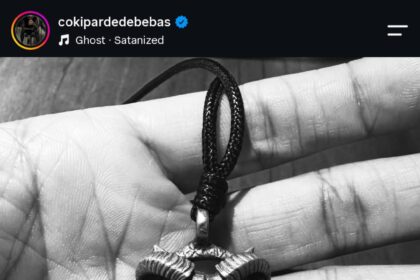 Metal ram-skull pendant on a black cord resting in a hand, shown in black and white.
