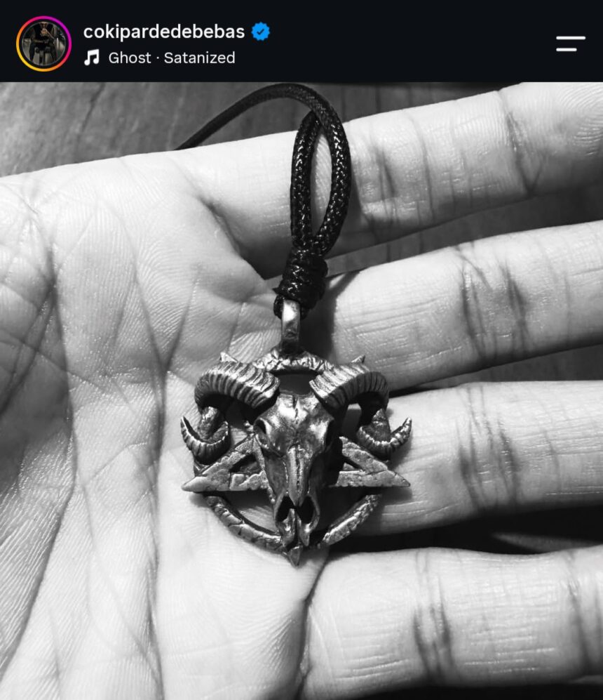 Metal ram-skull pendant on a black cord resting in a hand, shown in black and white.