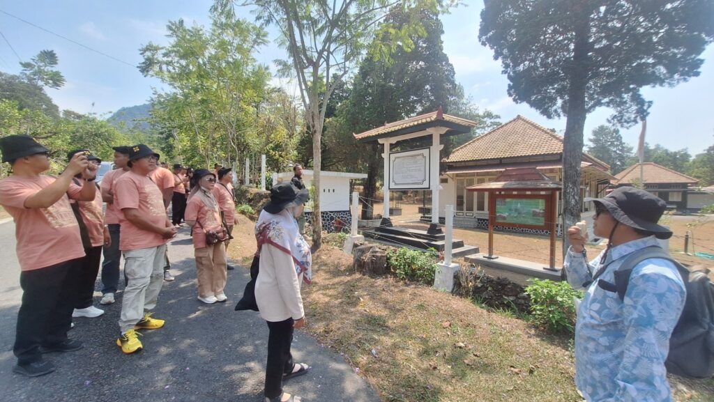 Screenshot_20260916_181809_Gallery - Mabur.co Tour group in matching peach shirts listens to a guide near a historical site with a signboard and small tiled-roof buildings.