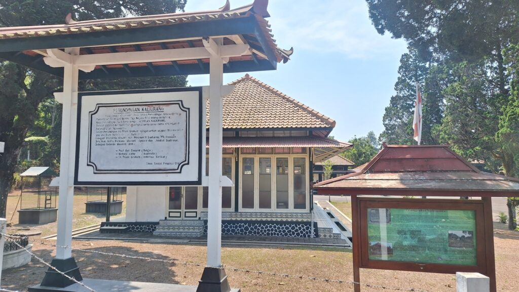 Traditional pavilion with tiled roof and a large signboard in front, Indonesian flag in the background.