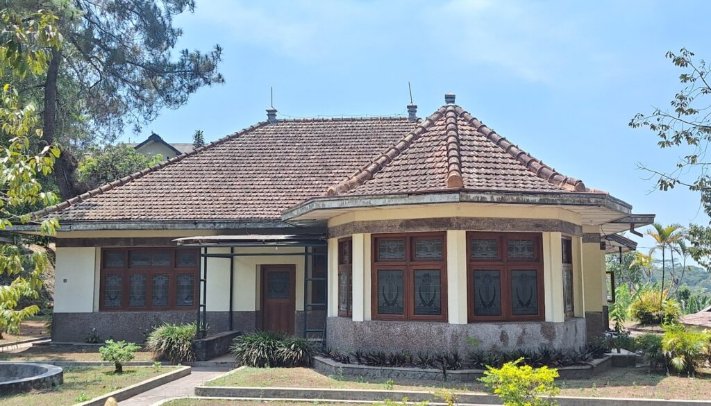 Screenshot_20260917_010135_Gallery - Mabur.co Single-story house with a red-tiled, multi-gabled roof and large front bay windows with decorative grilles, set in a yard with shrubs.