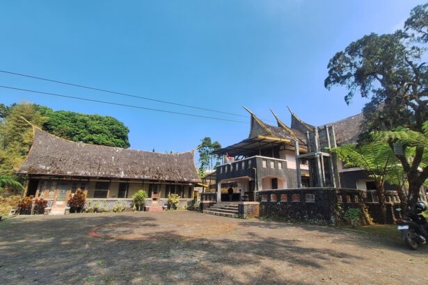 Courtyard scene with a long curved-roof traditional building on the left and a modern two-story structure on the right, under a clear blue sky.