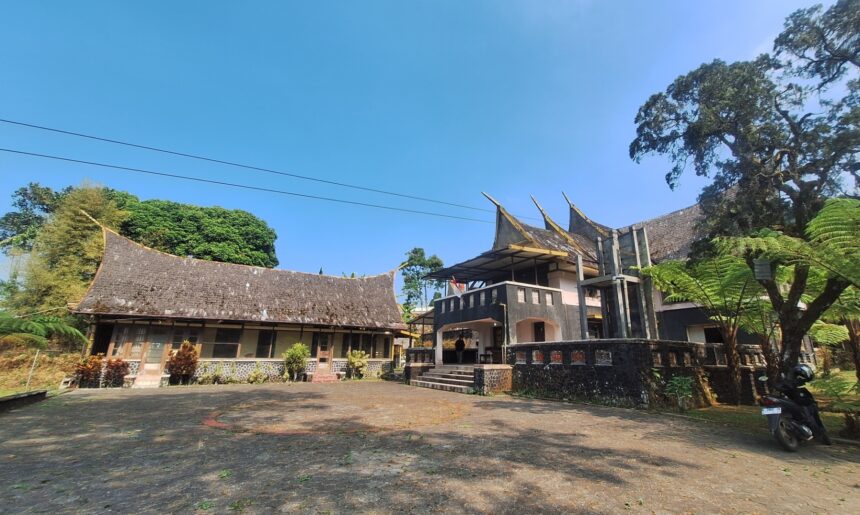 Courtyard scene with a long curved-roof traditional building on the left and a modern two-story structure on the right, under a clear blue sky.