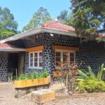 Stone-pattern cottage with a red tile roof, orange window awnings, and a lush garden in front.
