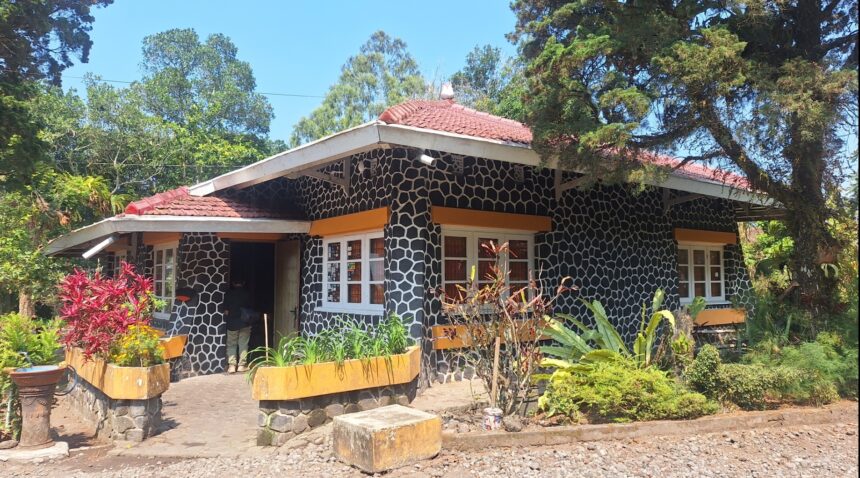 Stone-pattern cottage with a red tile roof, orange window awnings, and a lush garden in front.
