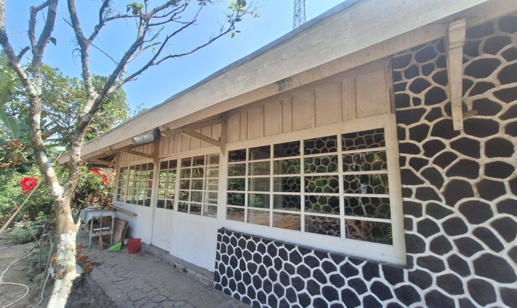 Front view of a single-story building with large pane windows and a black-and-white stone-pattern wall, in a sunny garden.