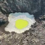 Aerial view of a volcanic crater with a neon yellow-green lake surrounded by jagged rocky walls.