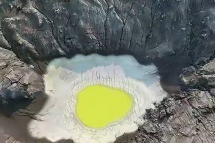 Aerial view of a volcanic crater with a neon yellow-green lake surrounded by jagged rocky walls.
