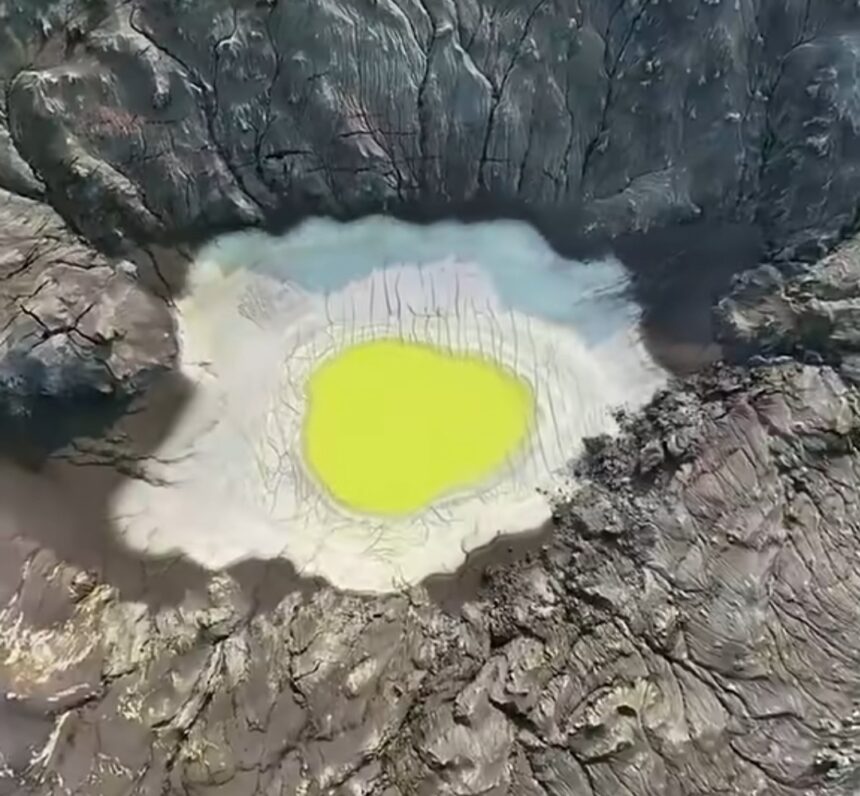 Aerial view of a volcanic crater with a neon yellow-green lake surrounded by jagged rocky walls.