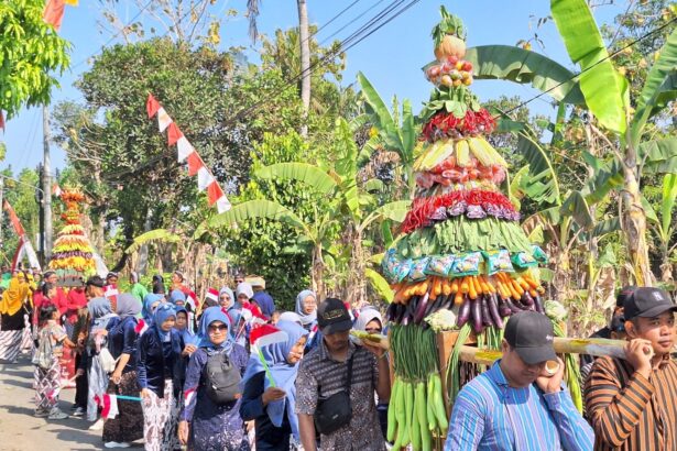 Colorful fruit-and-vegetable sculpture carried in a street festival, with onlookers in traditional clothing nearby.