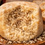 Round wheel of cheese with a hollowed center filled with pale mealworms, placed on a wooden board.