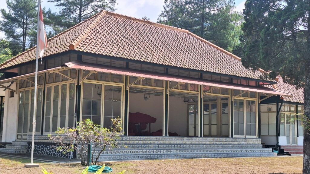 Screenshot_20260922_213801_Gallery - Mabur.co Glass-walled pavilion with a red tiled roof, decorative tiled base, and surrounding greenery in a park setting.