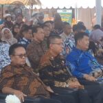 Group of people in batik shirts seated at an outdoor event, listening attentively under a tent.