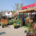 Outdoor market scene with white tents, a thatched-roof stall, and rows of potted plants and produce for sale.