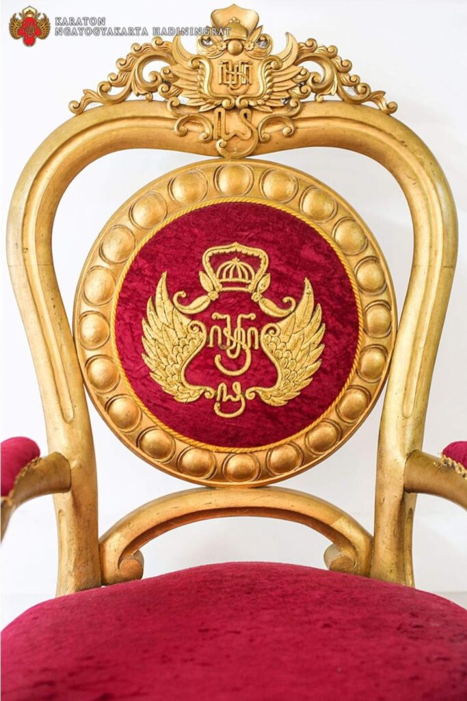 Screenshot_20261007_110549_X - Mabur.co Gilded ceremonial chair back with red velvet round emblem showing a gold crown and wings.