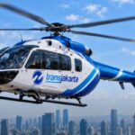 Blue and white Transjakarta helicopter in flight over a city skyline.