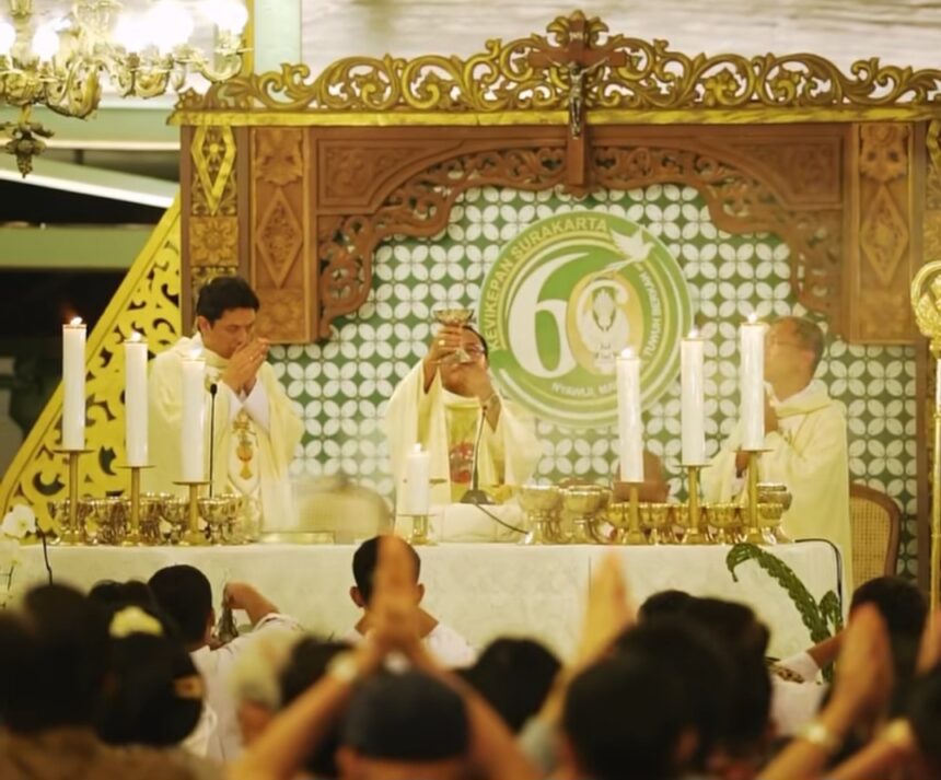 Priests in white robes perform a Catholic mass at an ornate altar, surrounded by lit candles and a gathered worshippers crowd.