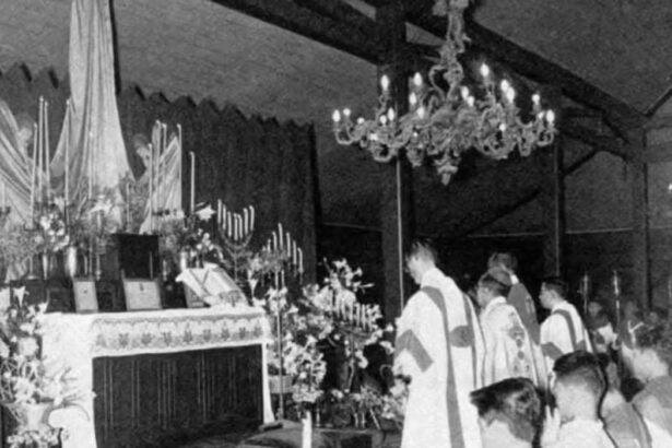 Priests in liturgical robes standing at an altar with candles and flowers during a church ceremony.