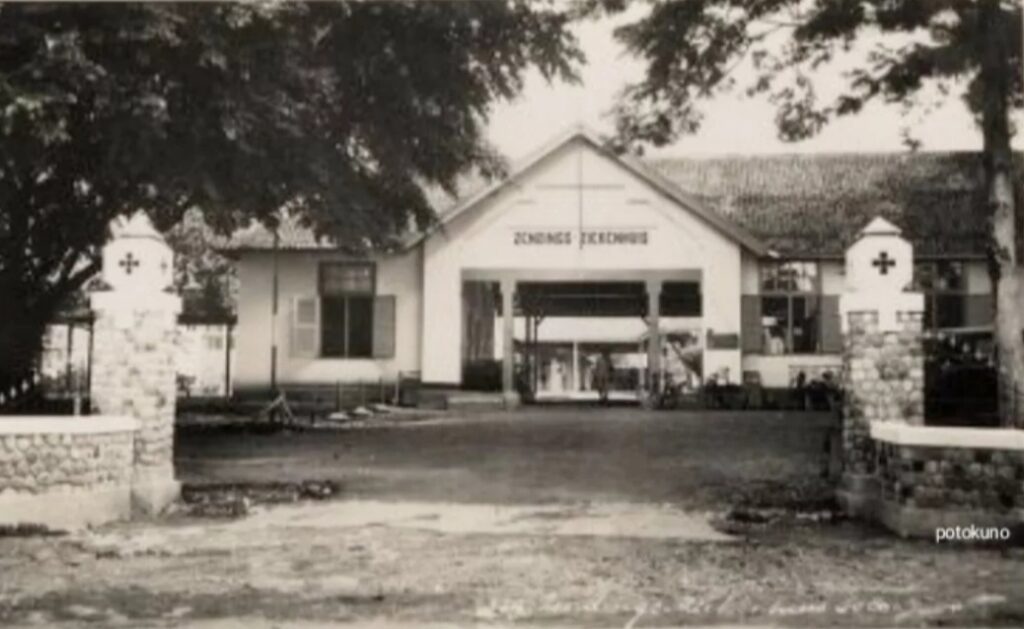 Screenshot_20261009_124131_Instagram - Mabur.co Vintage black-and-white photo of a single-story building with a central gabled entrance, flanked by stone gateposts and trees.