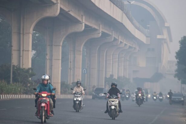 Motorcycles and cars ride on a hazy urban highway beneath a large elevated concrete overpass or viaduct, daytime traffic ahead.