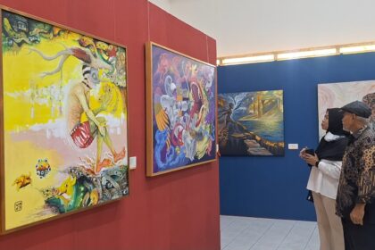 Two visitors stand side by side in an art gallery, admiring large colorful paintings on red and blue walls.