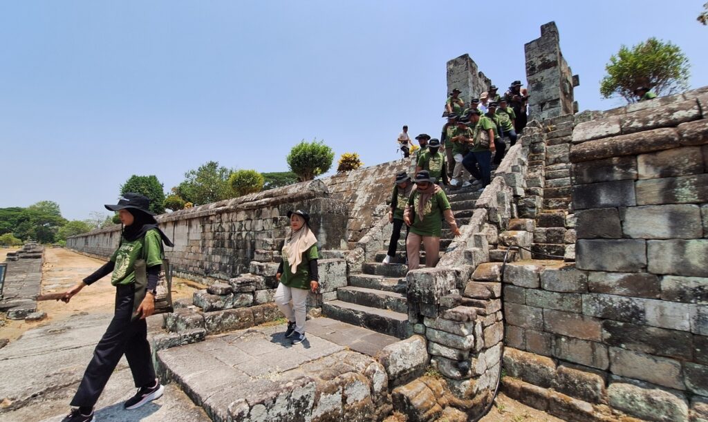 Tour group in matching green T-shirts descending ancient stone temple stairs under a clear blue sky.