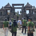 Tour group in green shirts ascending stone steps toward a large ancient temple gate under a blue sky