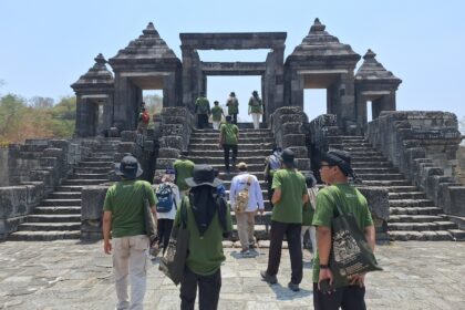Tour group in green shirts ascending stone steps toward a large ancient temple gate under a blue sky