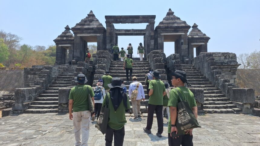 Tour group in green shirts ascending stone steps toward a large ancient temple gate under a blue sky