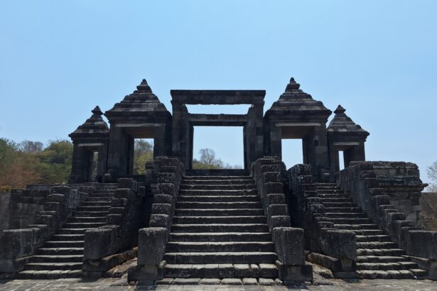 Ancient stone temple gateway with central opening, flanked by two pyramidal pavilions and broad stone stairs under a blue sky.