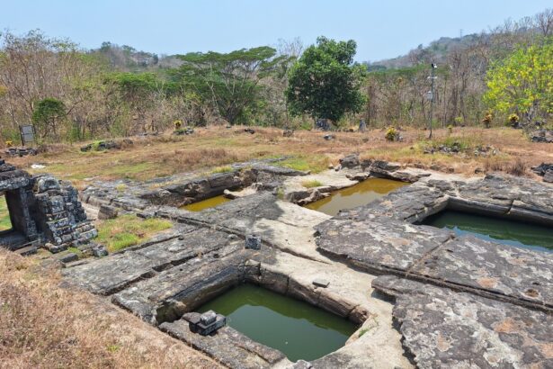 Ancient stone ruin with rectangular limestone basins filled with green water, set in dry grassy landscape and scattered stones.