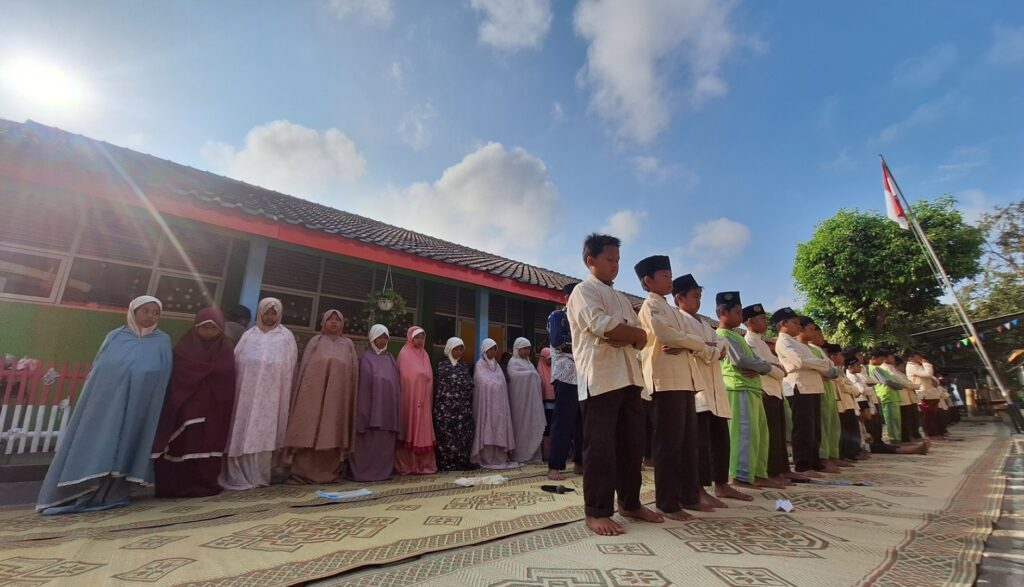 Group of students in traditional clothing standing in a row outdoors on woven mats, facing forward.