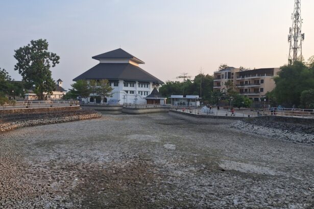 Riverside park with a tiered-roof white building, stone walls, and a boardwalk; people stroll along the water at dusk.