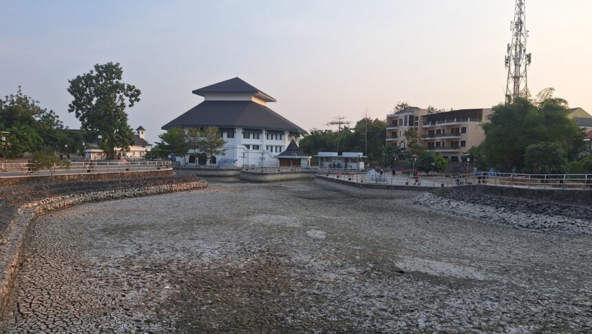 Riverside park with a tiered-roof white building, stone walls, and a boardwalk; people stroll along the water at dusk.