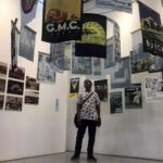Person standing in a gallery surrounded by hanging posters and wall-mounted photos/posters.