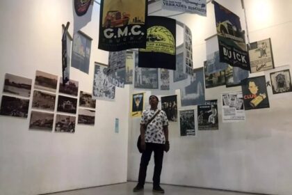 Person standing in a gallery surrounded by hanging posters and wall-mounted photos/posters.