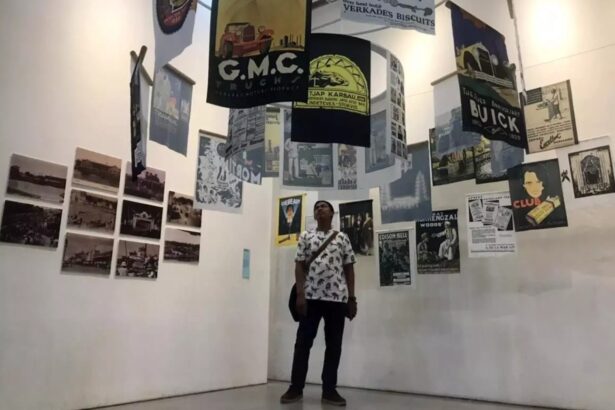 Person standing in a gallery surrounded by hanging posters and wall-mounted photos/posters.