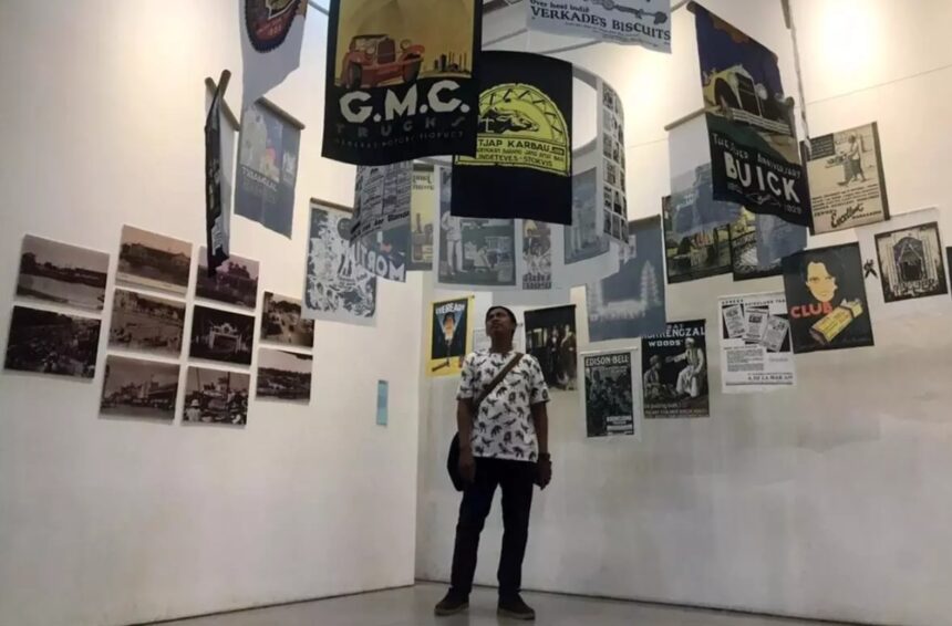 Person standing in a gallery surrounded by hanging posters and wall-mounted photos/posters.
