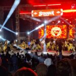 Stage at night with red lighting and a large screen reading 'Sitandi Fest'; dancers in gold and black costumes perform in front of a cheering crowd.