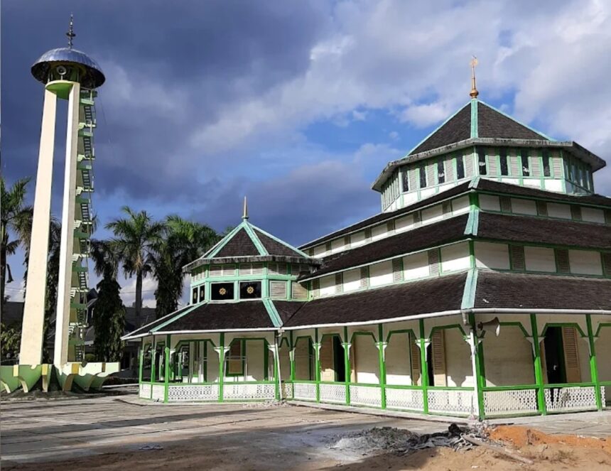 Green and white multi-tiered temple with a tall vertical tower on the left, palm trees in the background under a cloudy sky.
