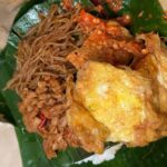 Crispy fried chicken served with stir-fried noodles on a banana leaf plate.