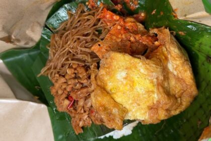 Crispy fried chicken served with stir-fried noodles on a banana leaf plate.