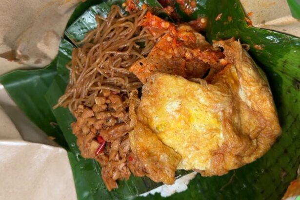 Crispy fried chicken served with stir-fried noodles on a banana leaf plate.
