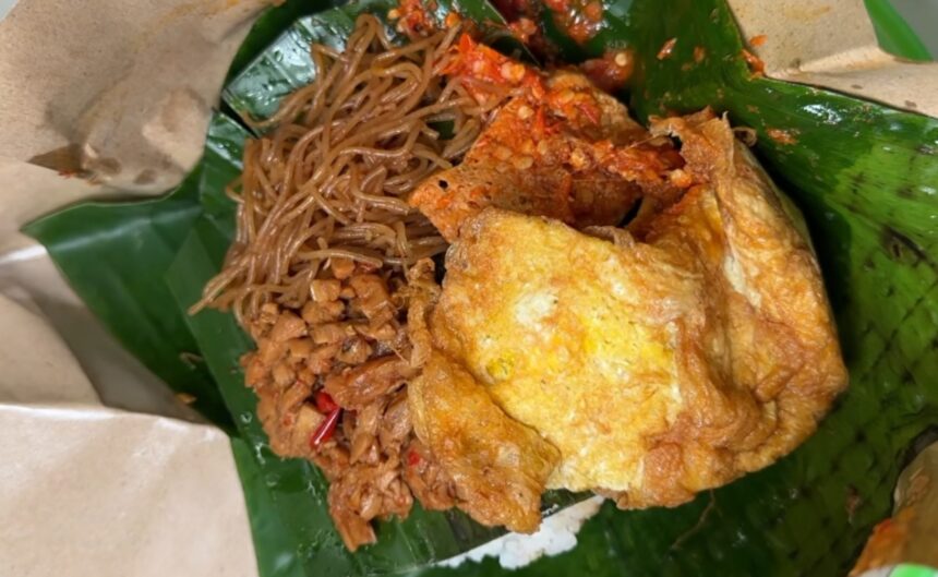 Crispy fried chicken served with stir-fried noodles on a banana leaf plate.