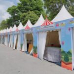 Row of blue festival stalls with white tents and red striped tops lined along a street for an outdoor fair or carnival.
