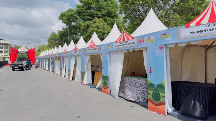 Row of blue festival stalls with white tents and red striped tops lined along a street for an outdoor fair or carnival.