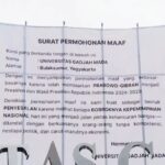 Large white banner titled 'SURAT PERMOHONAN MAAF' with Indonesian text, displayed outdoors with flag nearby, announcing an official apology.