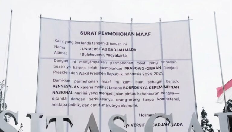 Sebuah spanduk jumbo berlatar putih bertuliskan “SURAT PERMOHONAN MAAF” mengatasnamakan UGM ter.heic - Mabur.co Large white banner titled 'SURAT PERMOHONAN MAAF' with Indonesian text, displayed outdoors with flag nearby, announcing an official apology.